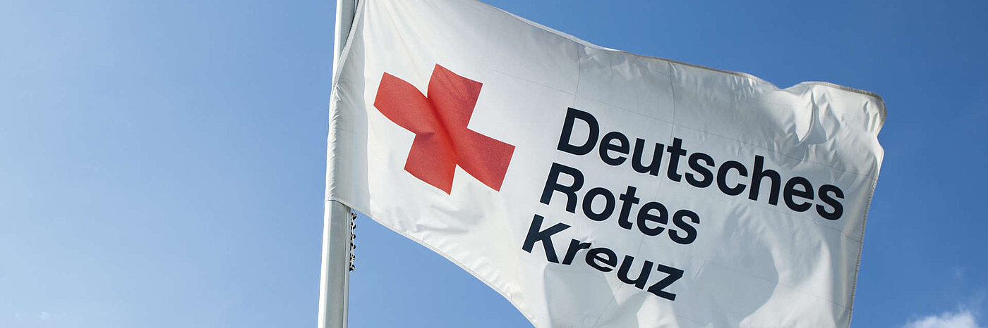 Das Logo des Deutschen Roten Kreuz auf einer Flagge vor blauem Himmel